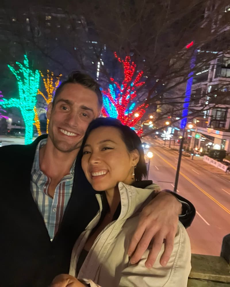 Matt and Anna at night in front of trees lit up in neon colours.