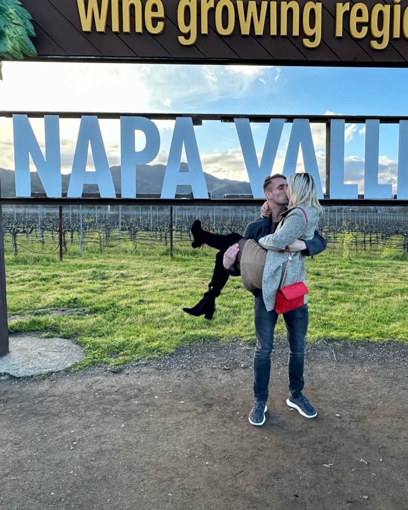 Matt carrying Anna in his arms in front of the Napa Valley sign.