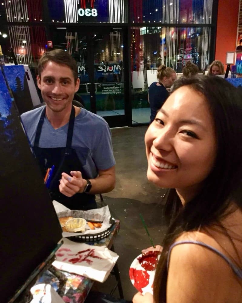 Matt in an apron and Anna smiling at a paint-and-sip class.