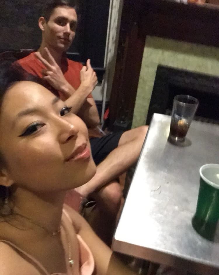 A selfie of Anna at a bar table, Matt behind her.