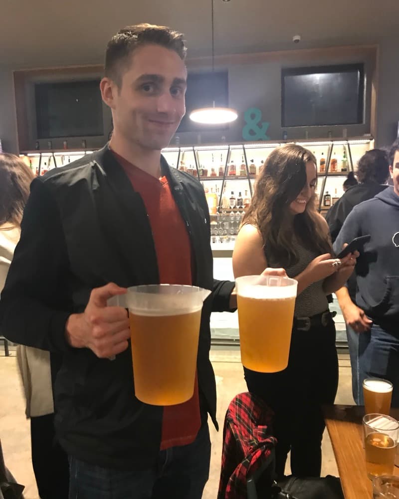 Matt holding two full pitchers of beer on a night out, Anna behind him.
